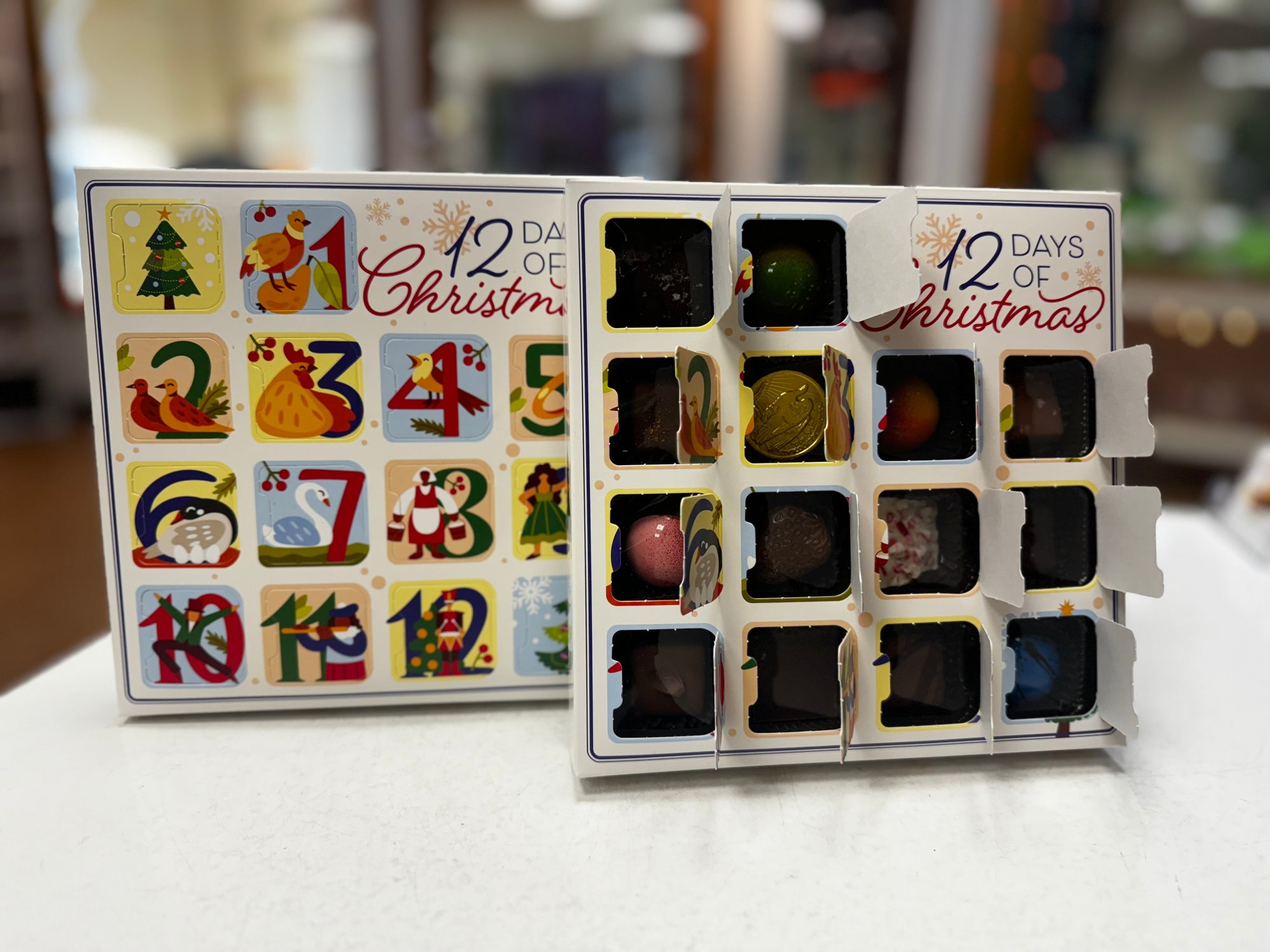 12 Days of Christmas calendar with small compartments on a white surface holding an assortment of chocolates and truffles