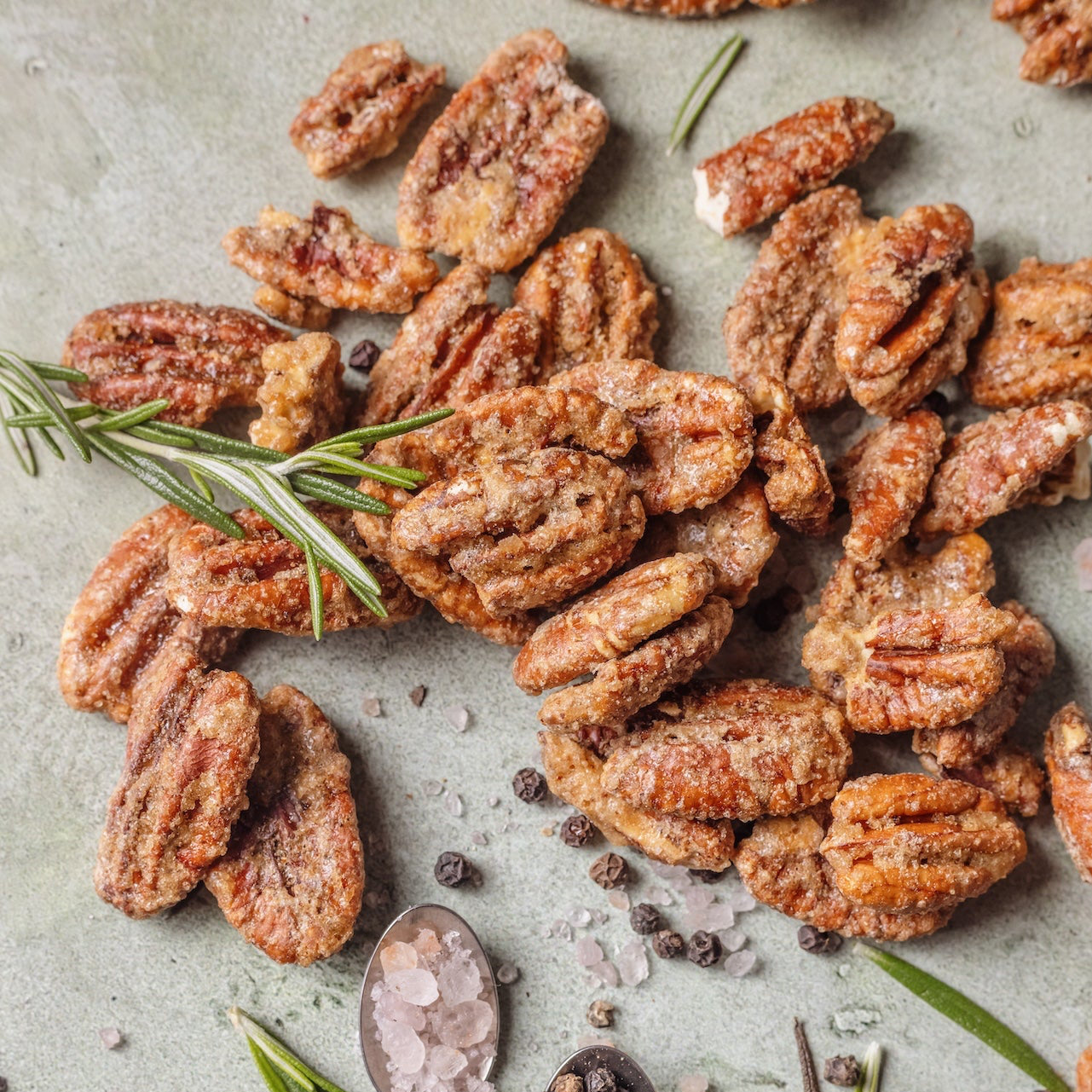 Spiced pecans with rosemary and a couple of spoons on a light surface