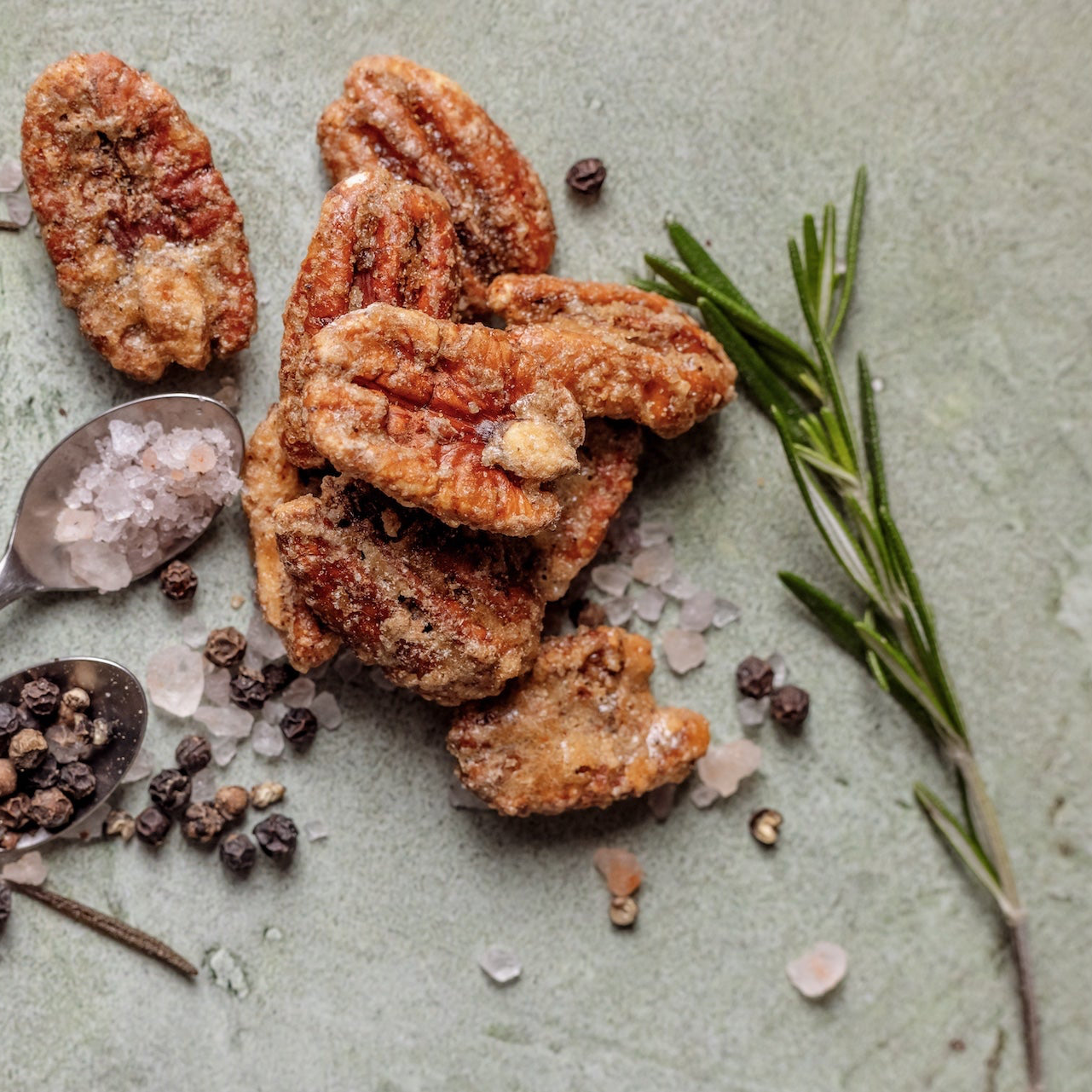 Pecans with rosemary, salt, and pepper on a textured surface