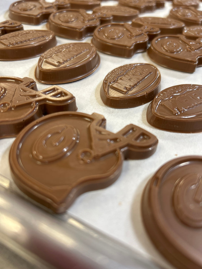 Close-up of several chocolate pieces shaped like football helmets, arranged on a light surface. The chocolates show embossed Green Bay football and helmet
