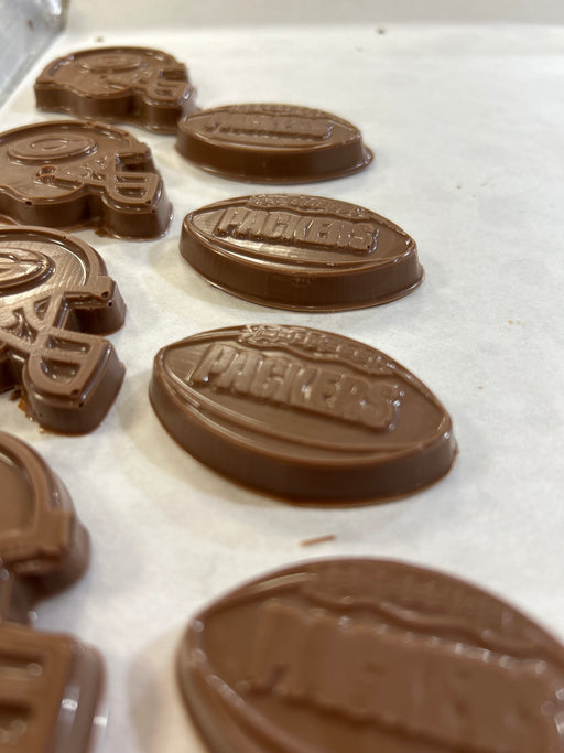 Several milk chocolate pieces shaped like football helmets and footballs, embossed with the word "PACKERS".