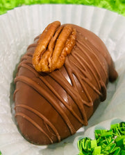 A chocolate Easter egg with a piece of pecan filling visible on top, coated in a brown chocolate shell.