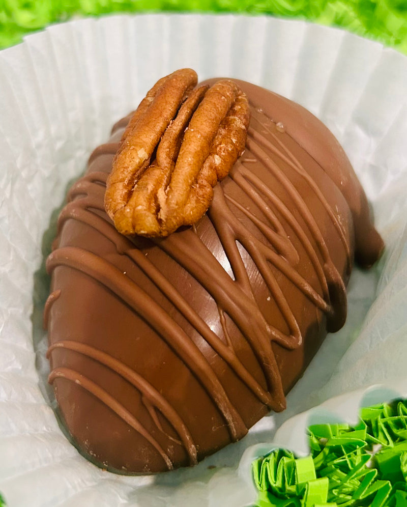 A chocolate Easter egg with a piece of pecan filling visible on top, coated in a brown chocolate shell.