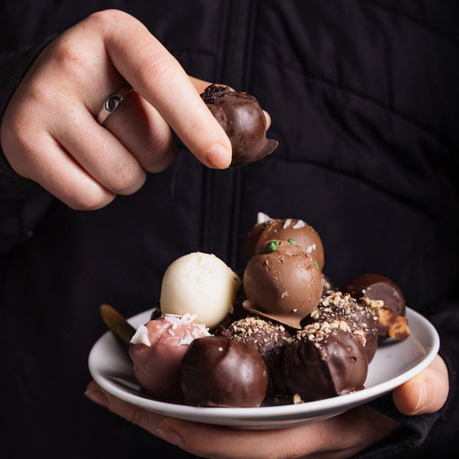 Person holding a plate of chocolate truffles against a dark background